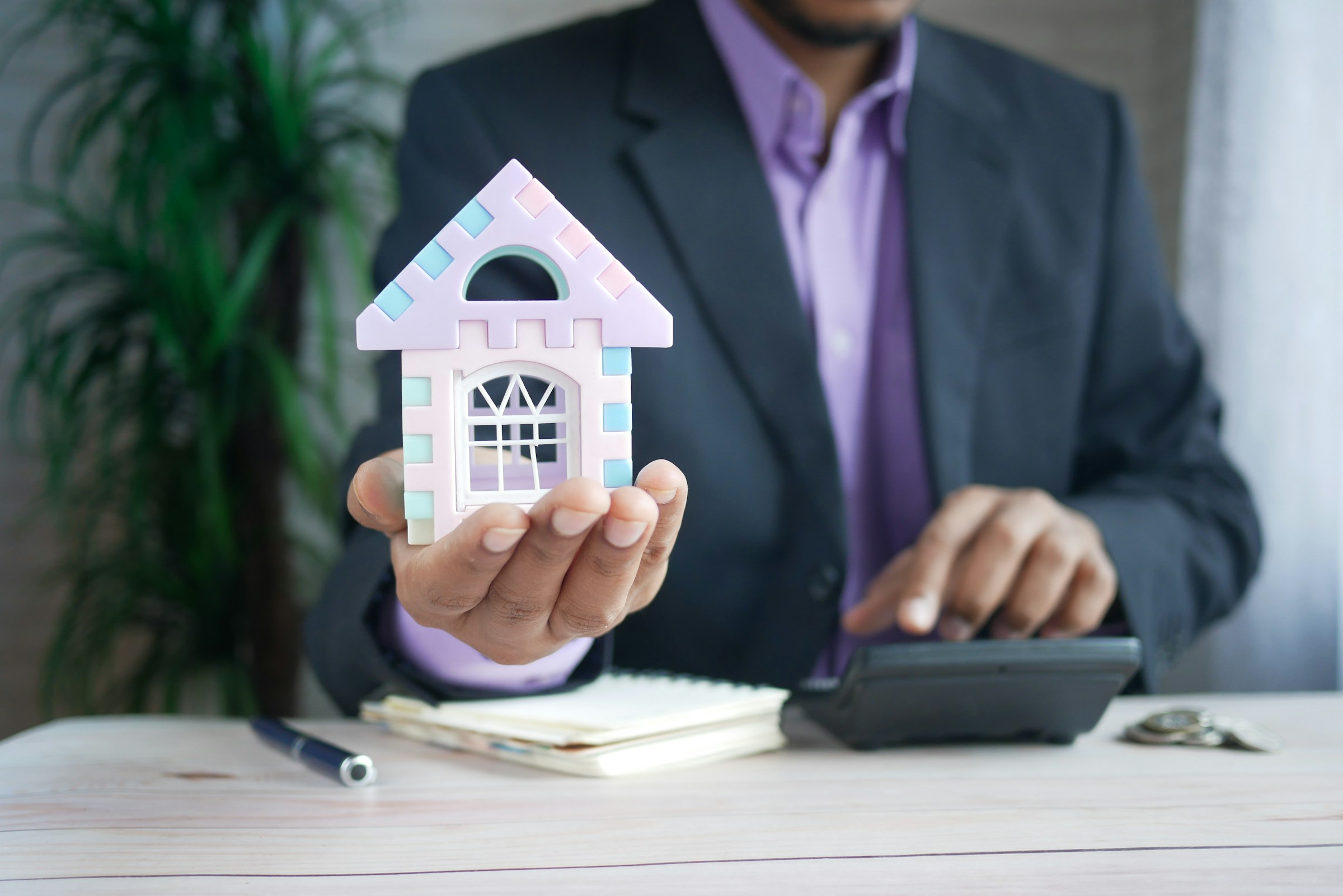 Homme en costume tenant une maison miniature, représentant l’acquisition pour investir en LMNP.