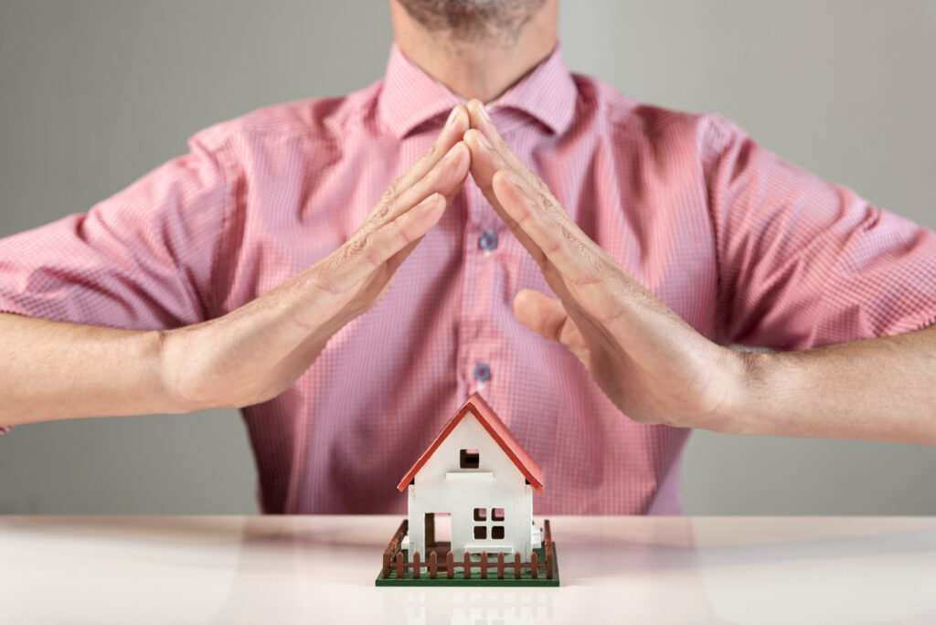 Homme protégeant une maison miniature avec ses mains symbolisant la sécurité en LMNP en nue-propriété