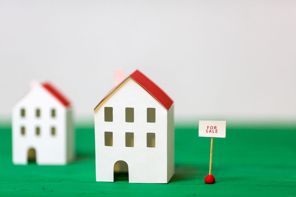 Maison en papier avec une pancarte "à vendre" illustrant une acquisition en LMNP en nue-propriété