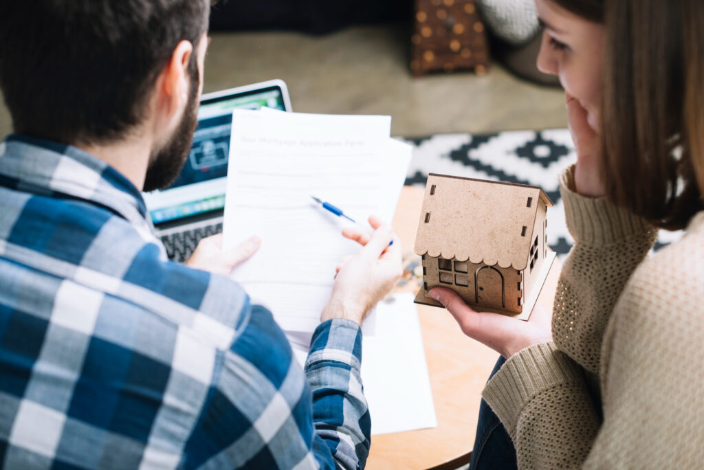 Couple étudiant un contrat immobilier avec une maison miniature pour un investissement en LMNP en nue-propriété