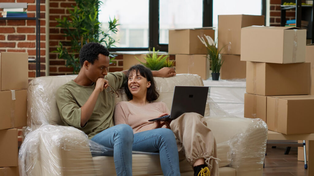 Couple assis dans un salon rempli de cartons, en pleine installation dans un logement pensé pour la colocation et la simulation LMNP en colocation.