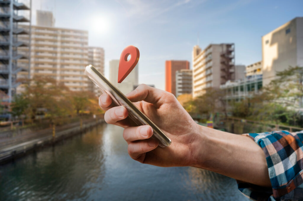 Main tenant un smartphone affichant un repère GPS devant des immeubles résidentiels modernes – contexte d'investissement locatif en LMNP à l’IS.