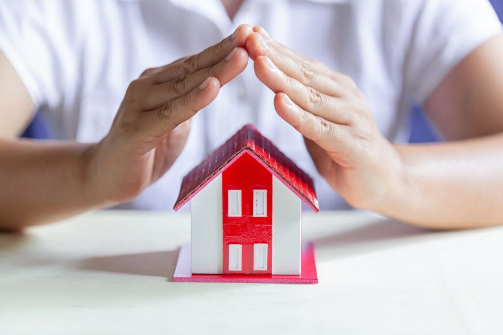 assurance loyers impayés LMNP symbolisée par des mains couvrant une maison miniature